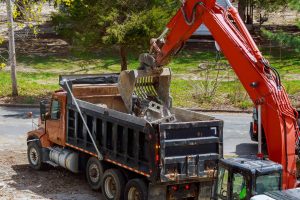 Excavator loading construction debris into truck during professional asbestos removal and certified disposal process
